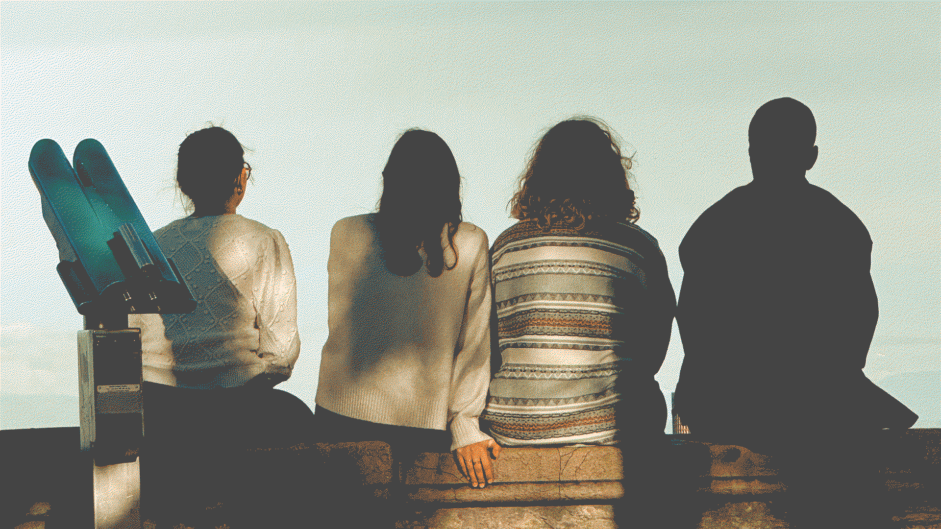 Four young people sat on a wall looking at the sky